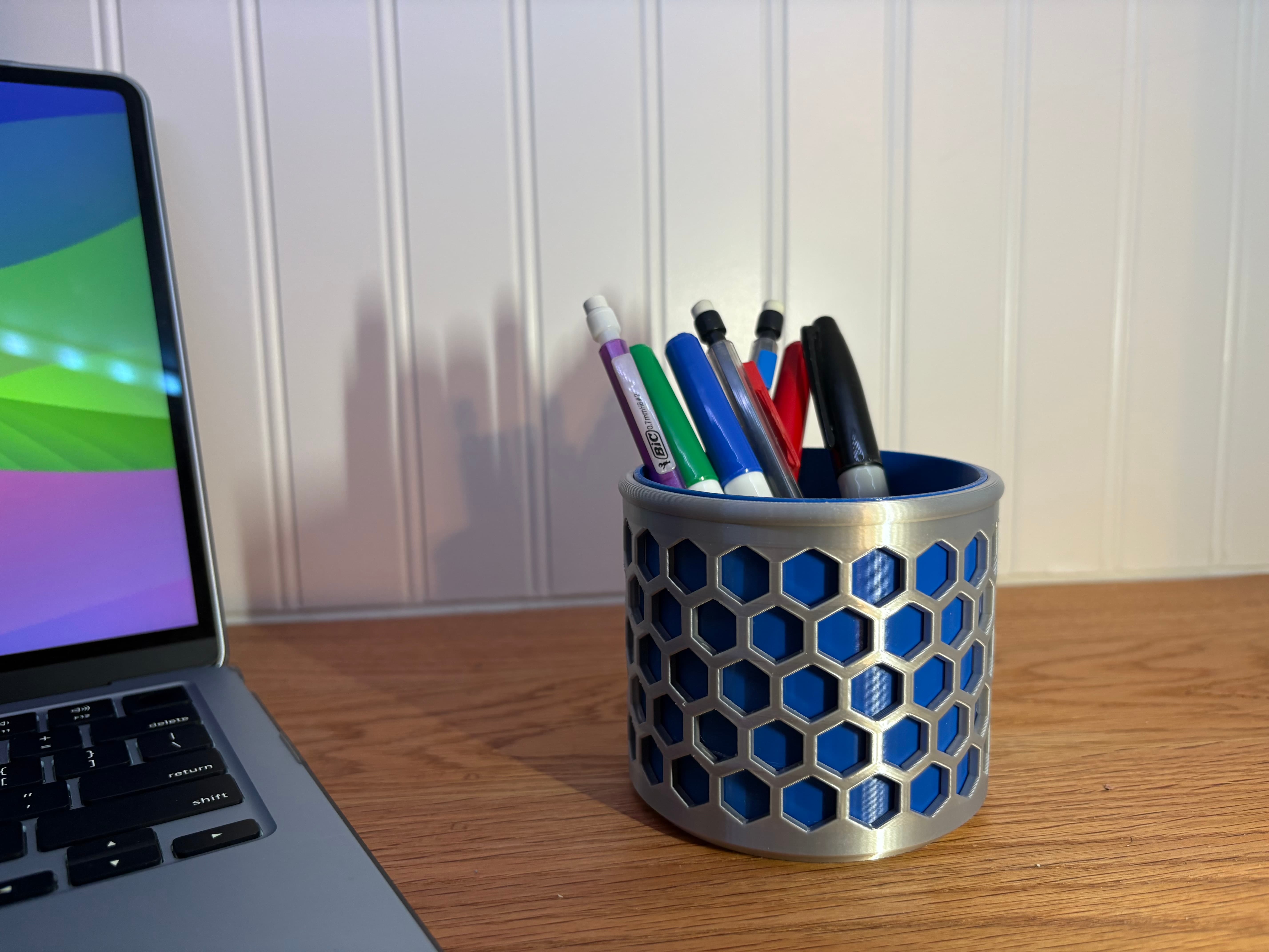 Silver and blue 3D printed honeycomb pencil holder filled with markers on a desk next to a laptop