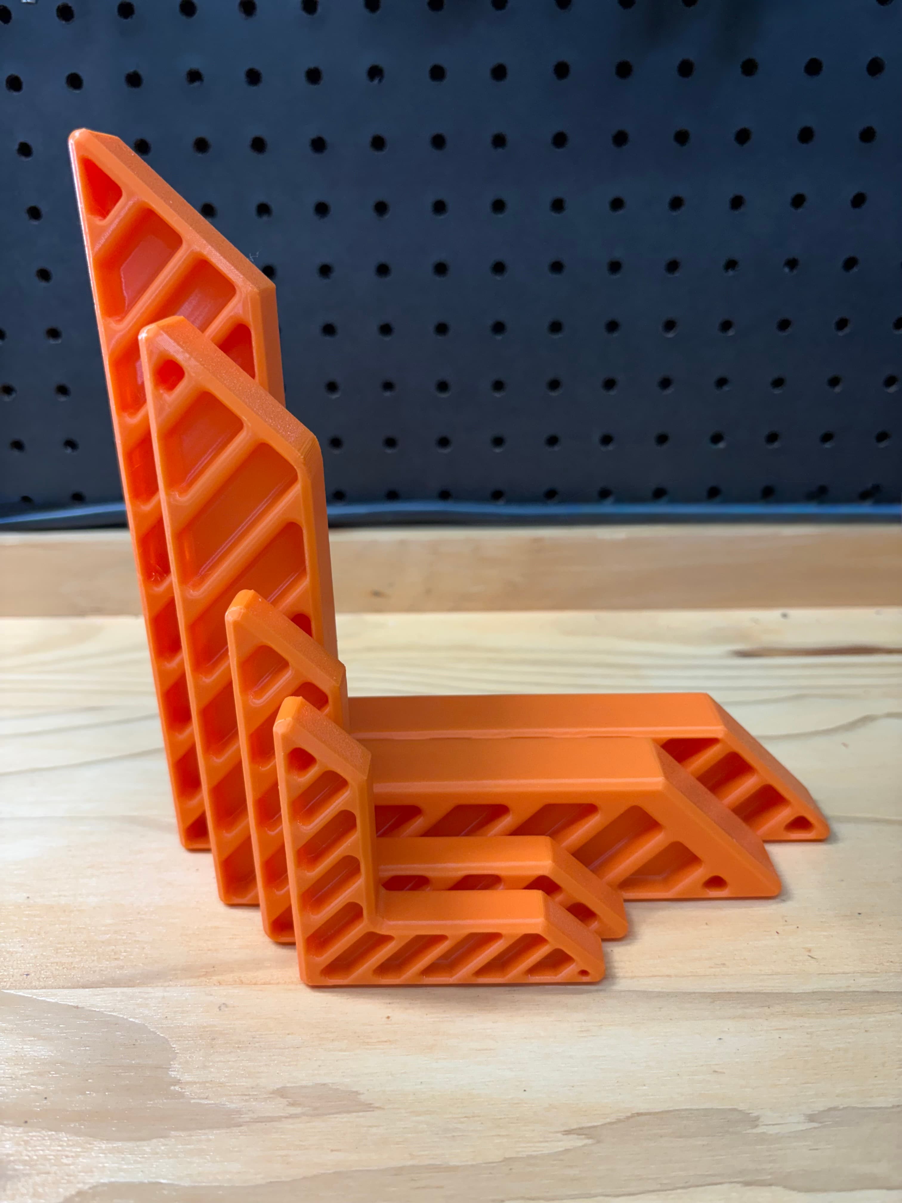 Set of four orange 3D printed woodworking clamping squares on a workbench
