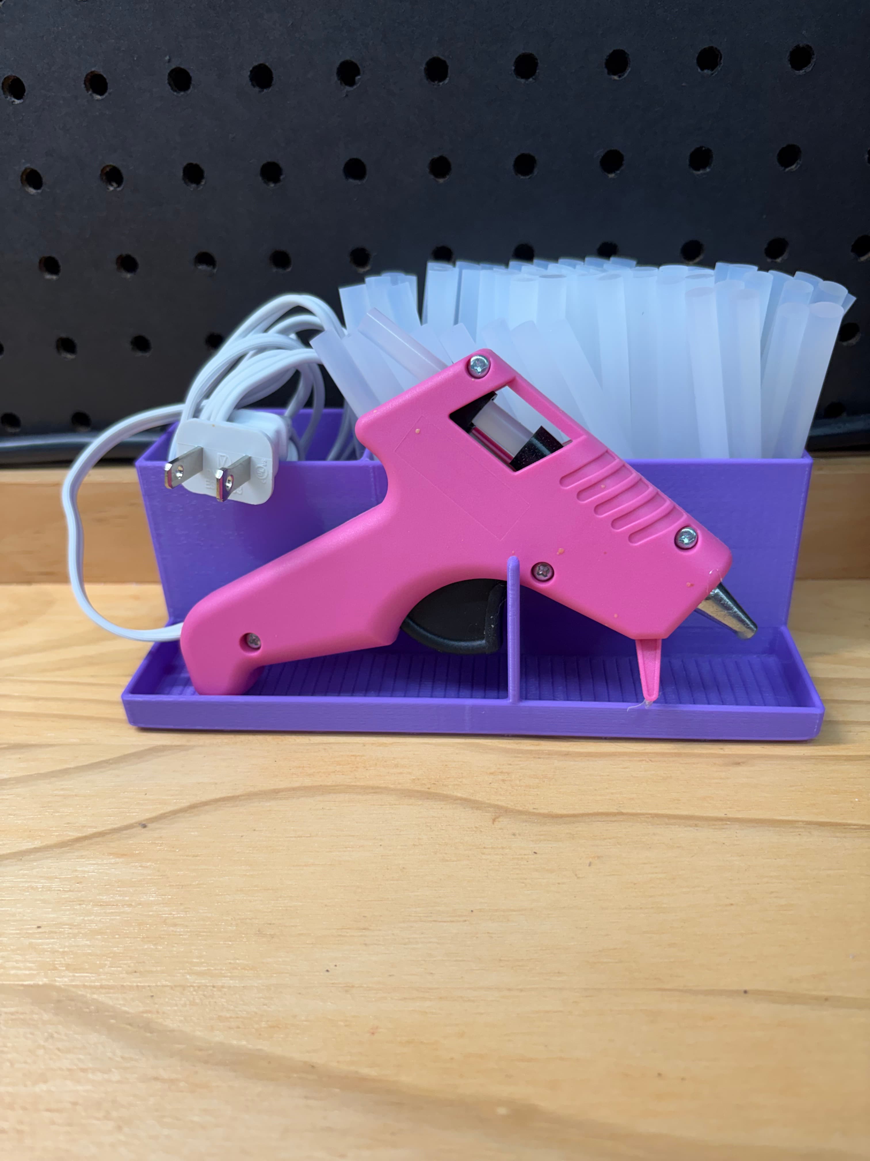 Purple 3D printed mini hot glue gun station holding a pink glue gun with glue sticks stored in back
