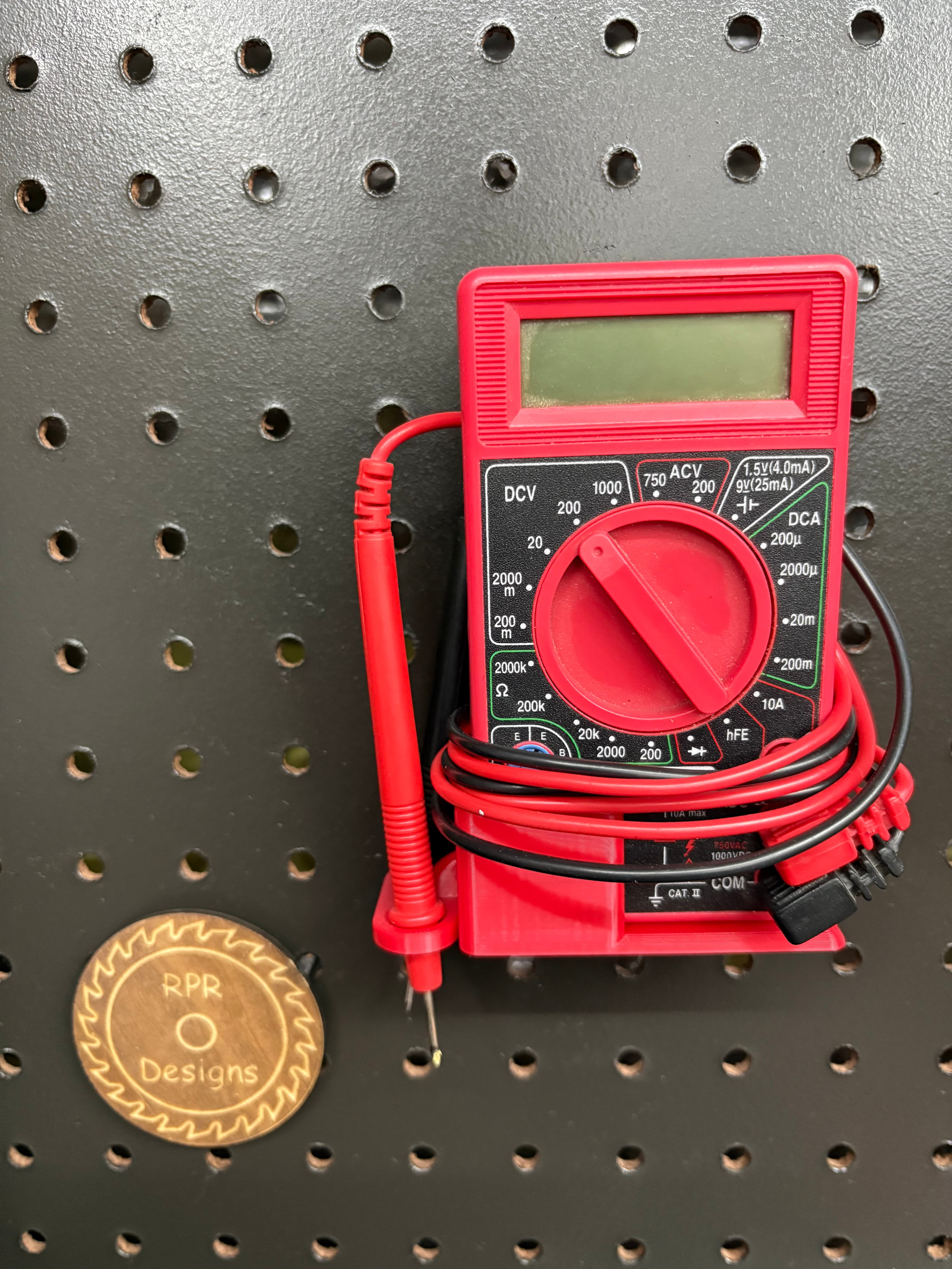 Red 3D printed multimeter holder mounted on a pegboard with lead storage loops