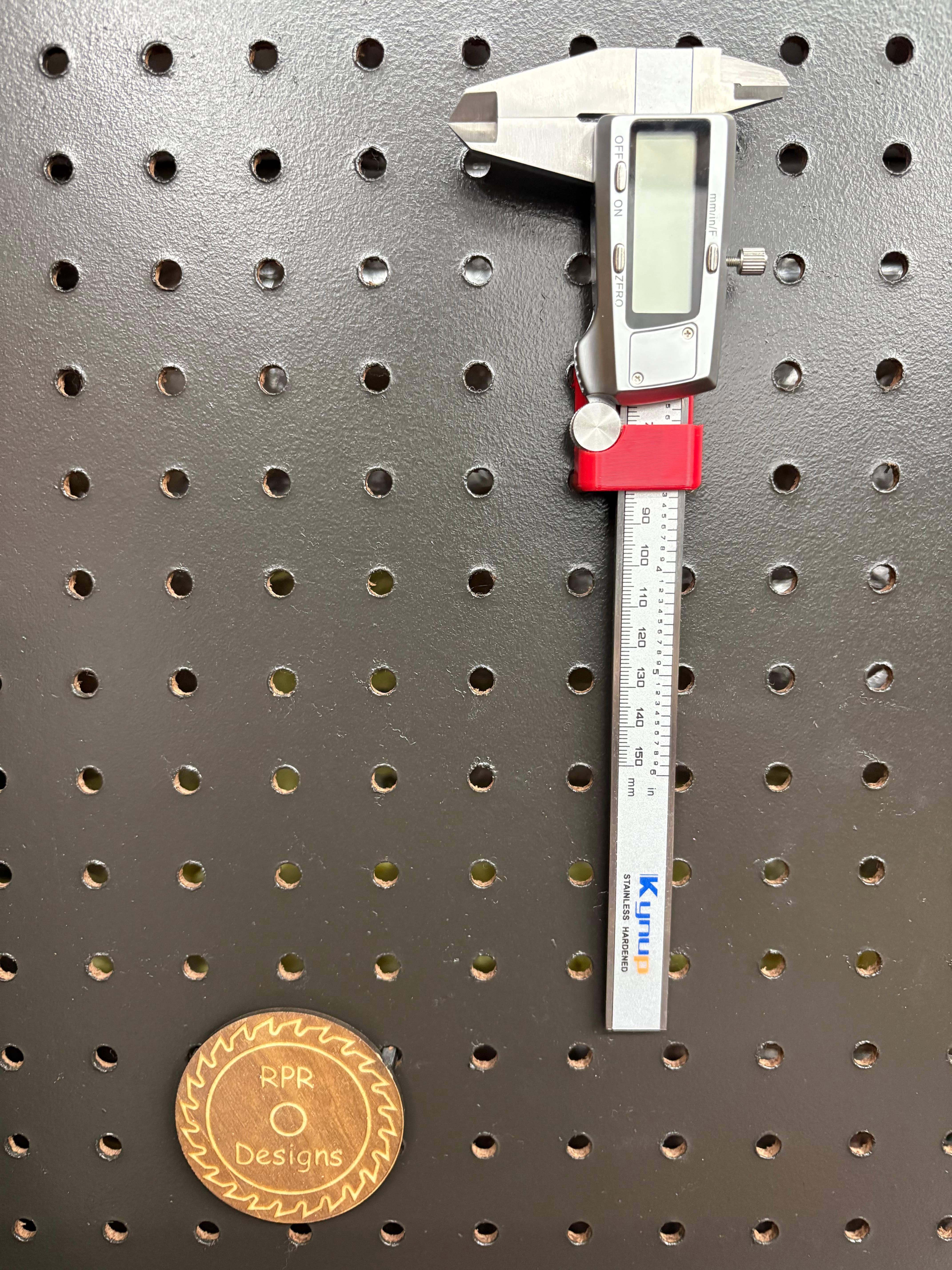 Red 3D printed digital caliper holder mounted on a pegboard